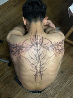 a man sitting on the floor with his back to the camera and tattoos on his chest