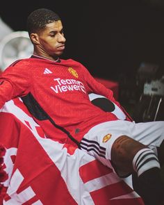 a man sitting on top of a soccer ball wearing a red shirt and white shorts