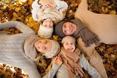 four people are laying in the leaves and posing for a photo with their arms around each other