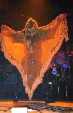 a woman in an orange dress on stage with her arms spread out to the side