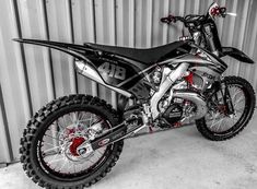 a black and white photo of a dirt bike parked in front of a metal wall