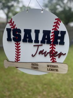 a sign for a baseball team hanging from a hook in the grass with a bat next to it