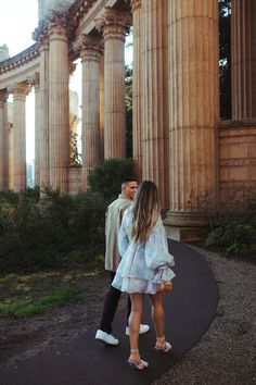 a man and woman standing in front of an old building with columns on either side