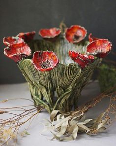 some red flowers are in a vase on a white tablecloth with dried plants and twigs