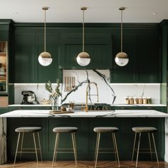 a kitchen with green cabinets, marble counter tops and gold pendant lights hanging from the ceiling