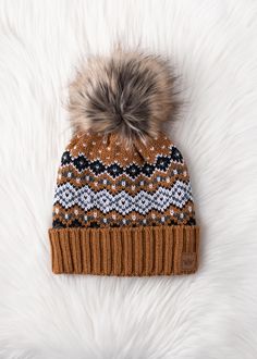 Camel, black, white and blue patterned knit pom hat Cuff detail at the hemline Natural faux fur pom accent Fleece lined Crown patch on the left side One size 100% Acrylic Winter Hats With Faux Fur Trim, Cozy Brown Beanie For Winter, Brown Cozy Winter Beanie, Cozy Brown Winter Beanie, Nordic Warm Beanie For Cold Weather, Casual Winter Hat With Faux Fur Trim, Warm Nordic Beanie For Cold Weather, Beanie With Faux Fur Trim For Cold Weather, Winter Hat With Pom Poms For Cold Weather