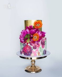 a multi - tiered cake decorated with flowers on a gold plated metal stand