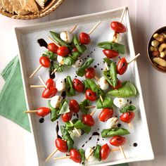 a white plate topped with skewers of food next to a bowl of nuts