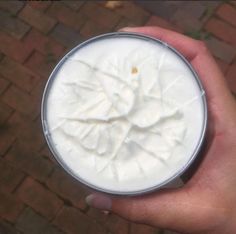 a hand is holding a cup with whipped cream in it on a brick patio area