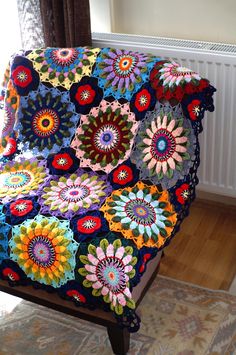 a multicolored crocheted blanket sitting on top of a chair in front of a window