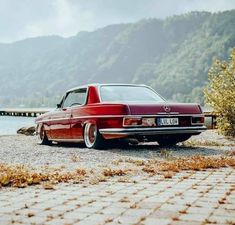 an old red car parked next to a body of water