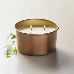 a candle that is sitting on a table next to some white flowers and green leaves