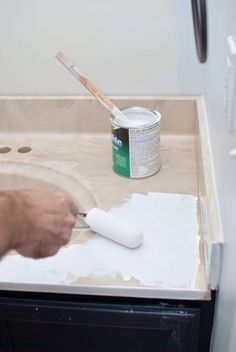 a person is using a brush to paint the base of a sink with white paint