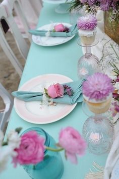 the table is set with pink flowers and blue vases, plates and napkins