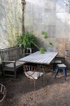 an outdoor table and chairs are set up in front of a wall with plants on it