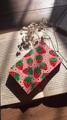 an open book sitting on top of a wooden table next to a plant and flowers