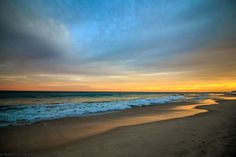 the sun is setting at the beach with waves coming in