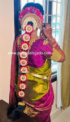 a woman in a purple and green sari is talking on her cell phone while standing near a window