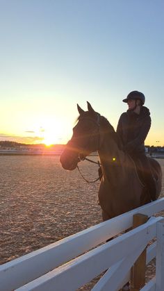 a woman riding on the back of a brown horse next to a white wooden fence