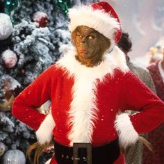 a man dressed as santa claus standing in front of a christmas tree with his hands on his hips