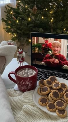 a laptop computer sitting on top of a table with cookies and hot chocolate in front of it