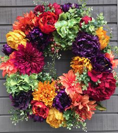 a colorful wreath is hanging on the side of a building with purple, orange and red flowers