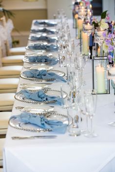 a long table is set with silverware, candles and blue napkins on it