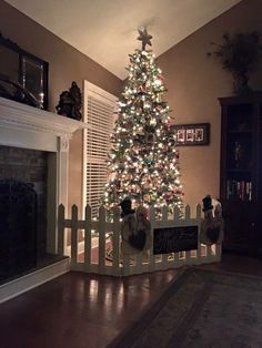 a christmas tree is lit up in a living room with a white picket fence around it