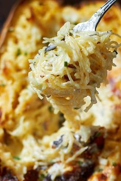 a spoon full of macaroni and cheese being lifted from a casserole dish