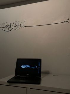 an open laptop computer sitting on top of a white desk next to a wall with arabic writing