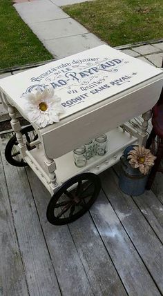 a white cart with flowers on it sitting on the side of a wooden floor next to a sidewalk