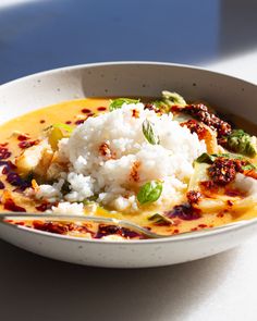 a white bowl filled with rice and vegetables on top of a table next to a spoon