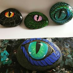 three painted rocks sitting on top of a white counter next to each other with green and blue eyes