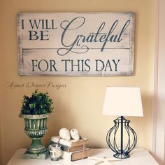 a white table topped with a lamp next to a sign that says i will be grateful for this day