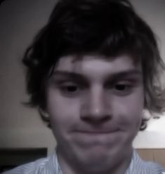 a man with long hair is smiling at the camera while wearing a blue and white striped shirt