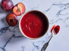 a bowl filled with red liquid next to two pieces of fruit on a marble counter top