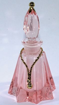 a pink glass perfume bottle sitting on top of a white table next to a gold chain