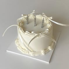 a small white cake with three candles on it and ribbon around the top, sitting on a card