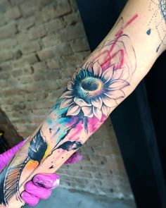 a person with a tattoo on their arm holding onto a piece of art that looks like a sunflower