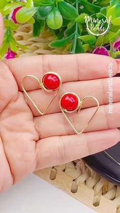 two heart shaped earrings with red stones in the middle, on top of a person's hand