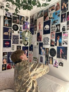 a young boy sitting on top of a bed next to a wall covered in pictures