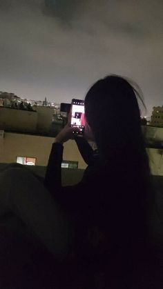 a woman taking a photo with her cell phone at night on top of a building