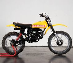 a yellow dirt bike parked on top of a hard wood floor next to a white wall