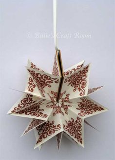 an origami star decoration hanging from a white string with red designs on it