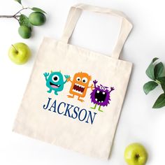 a personalized tote bag with two monsters and an apple on the table next to it