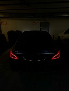 the back end of a black sports car in a parking garage with its lights on