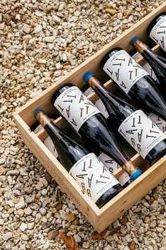 several bottles of wine in a wooden box on the ground next to rocks and pebbles