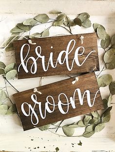 two wooden signs with the words bride and groom painted on them, surrounded by greenery