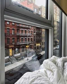 an unmade bed sitting in front of a window next to a tall building with lots of windows