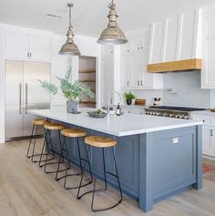 a kitchen island with four stools in front of it and two lights hanging from the ceiling